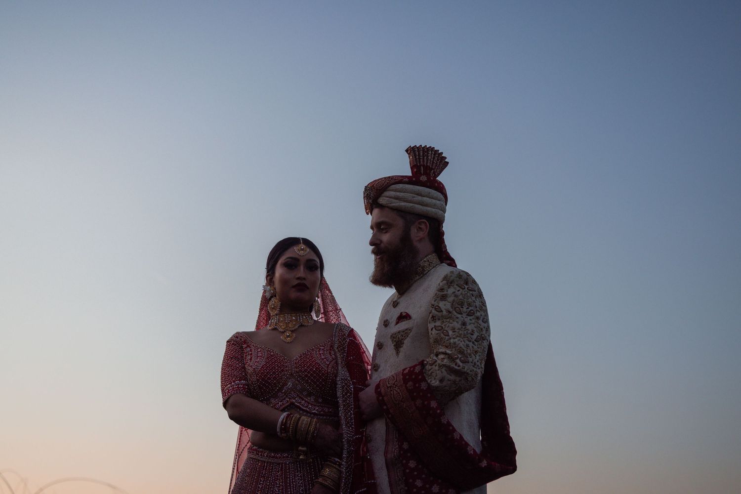 Silhouettes of people standing against a sunset sky during a mountaintop proposal moment.