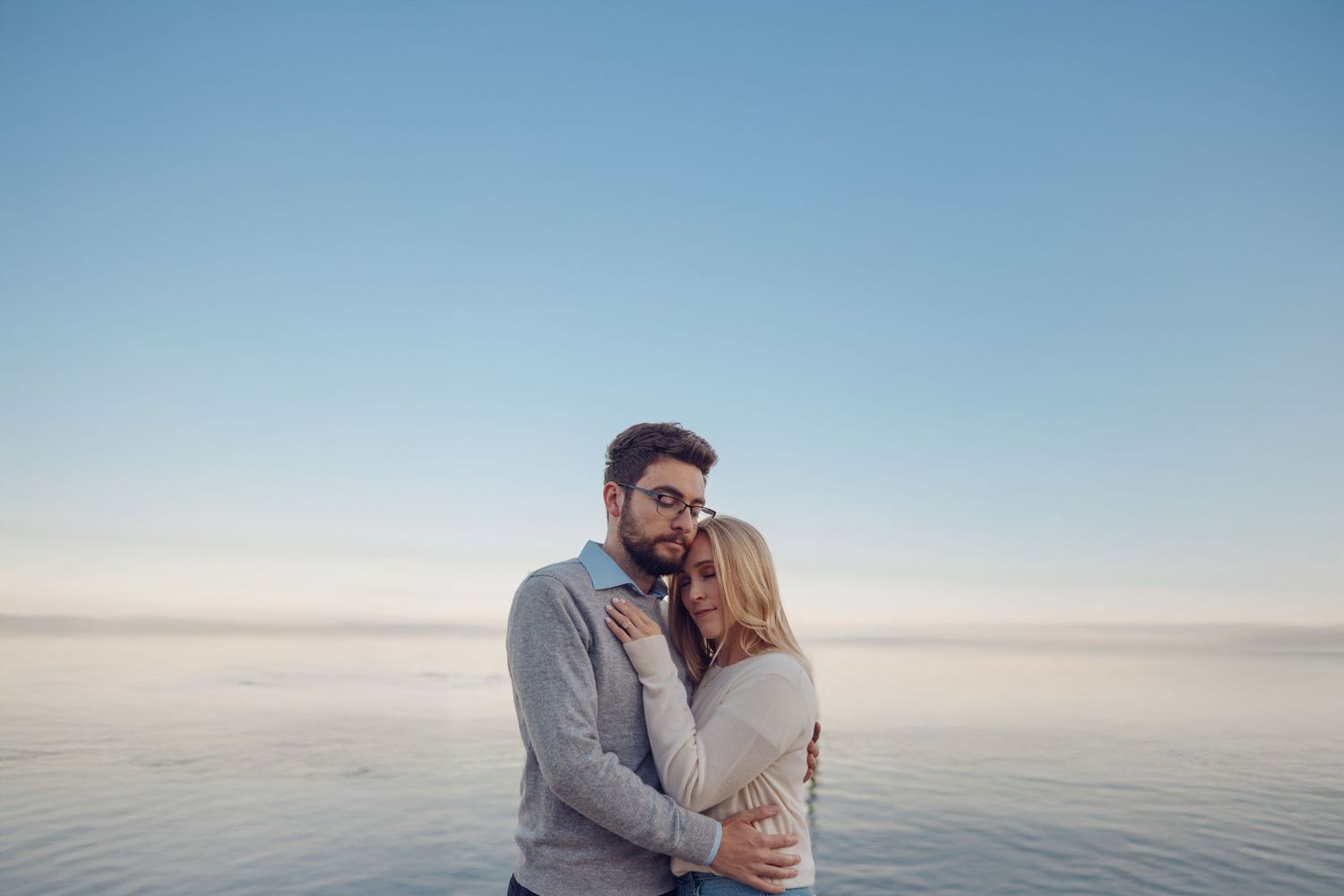 Couple embracing against serene waterfront backdrop during golden hour.