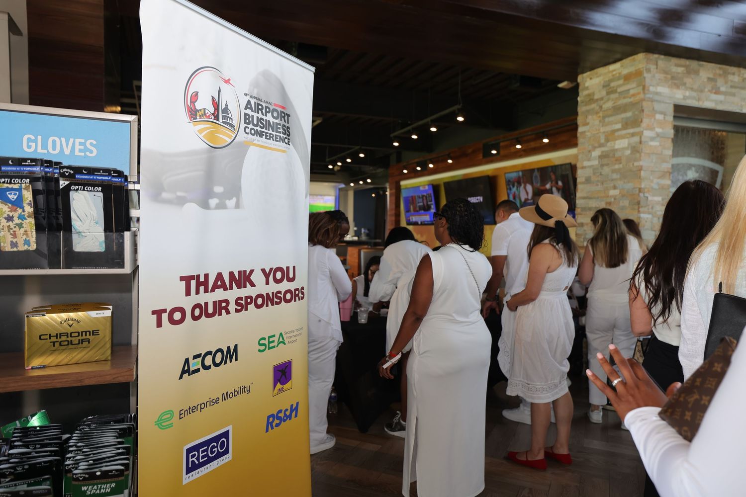 Sponsors thank you banner at Airport Summit event with guests dressed in white attending the networking reception.