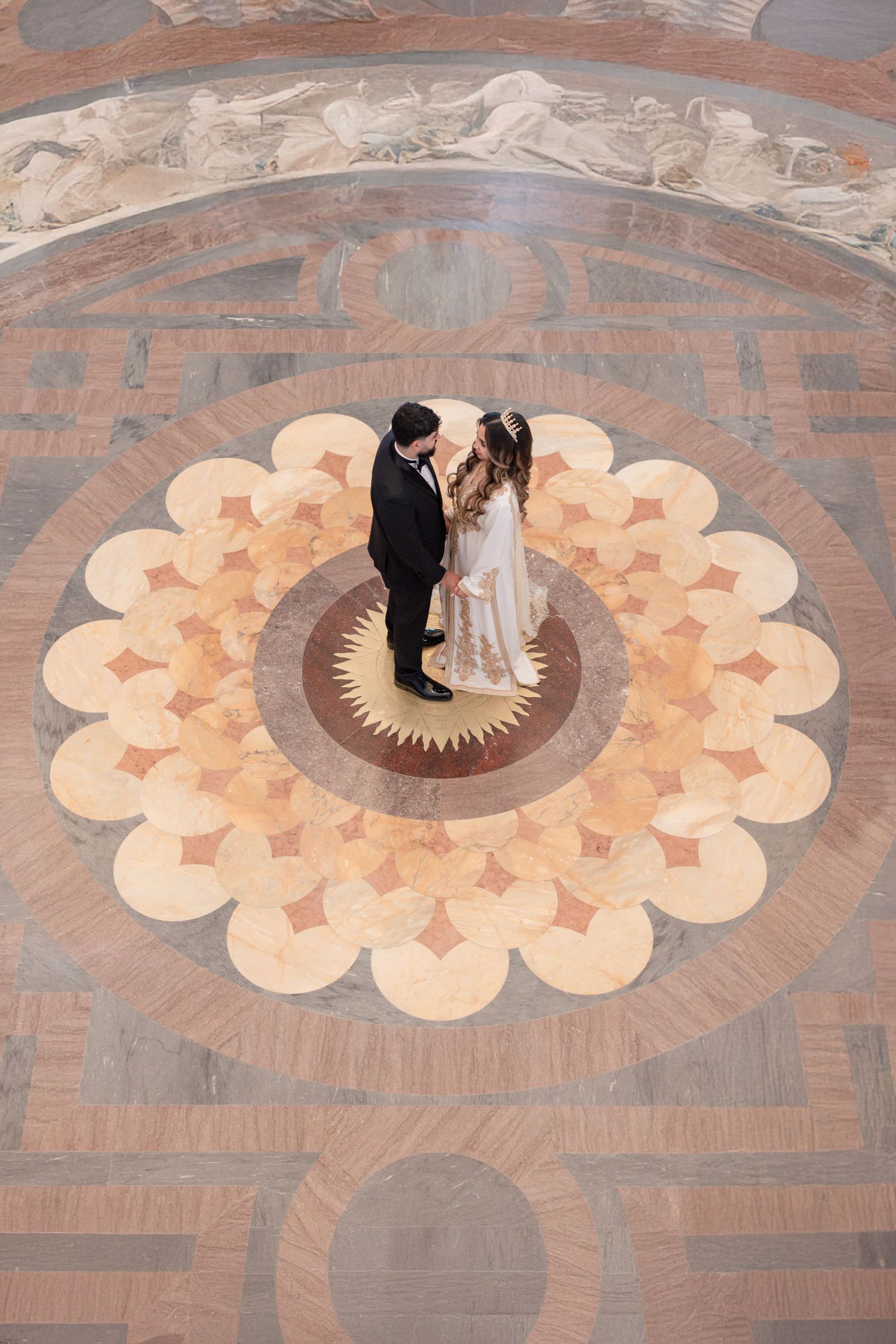 Two people dance in a circular pattern on an ornate marble floor with a geometric sunburst design.