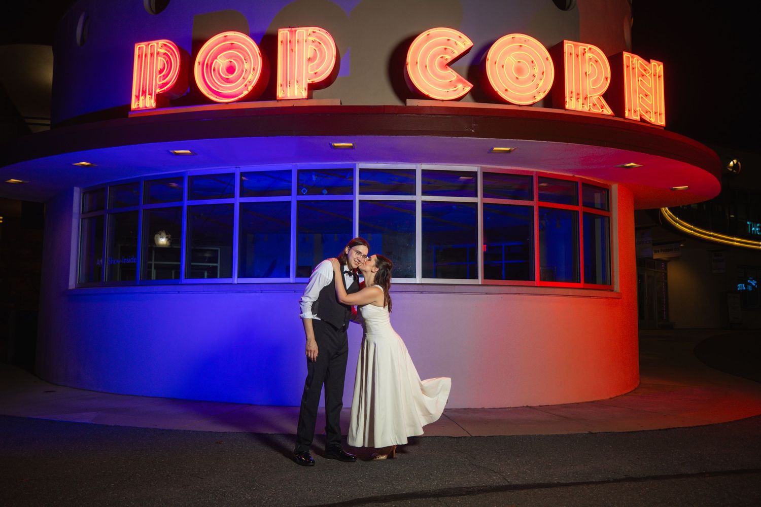 Illuminated red neon popcorn sign glows brightly against dark background at retro movie theater entrance.