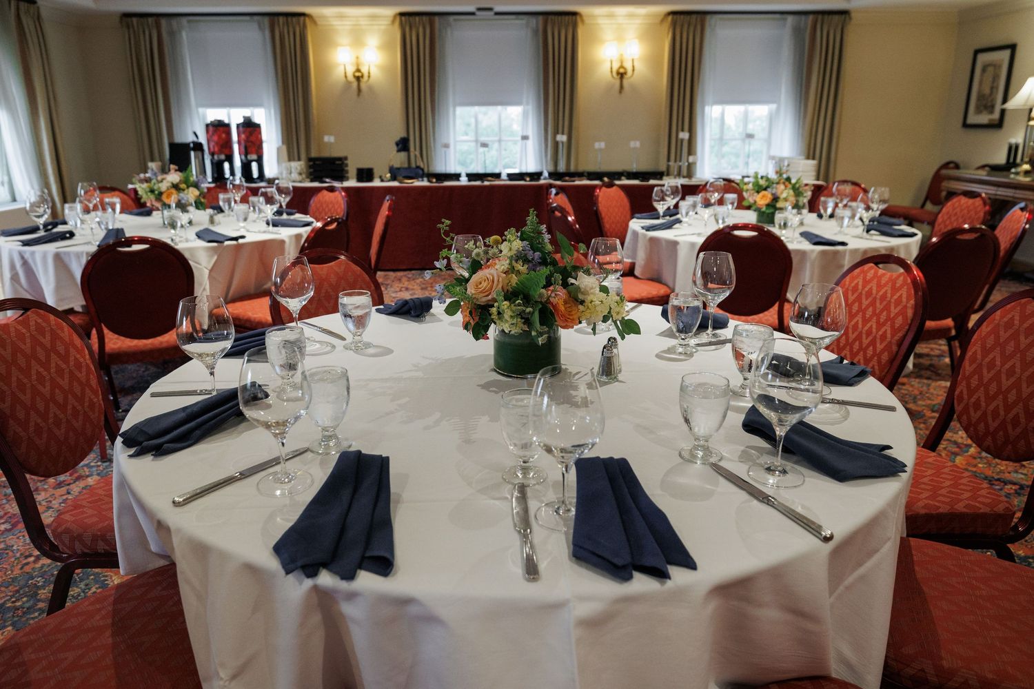 Elegant banquet hall with round tables set for a formal dinner, featuring white linens, navy napkins, and floral centerpieces.