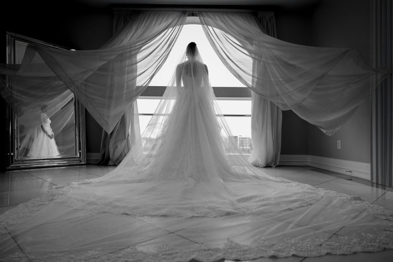 A dramatic black and white photo of a bride in a flowing veil silhouetted against a bright window.