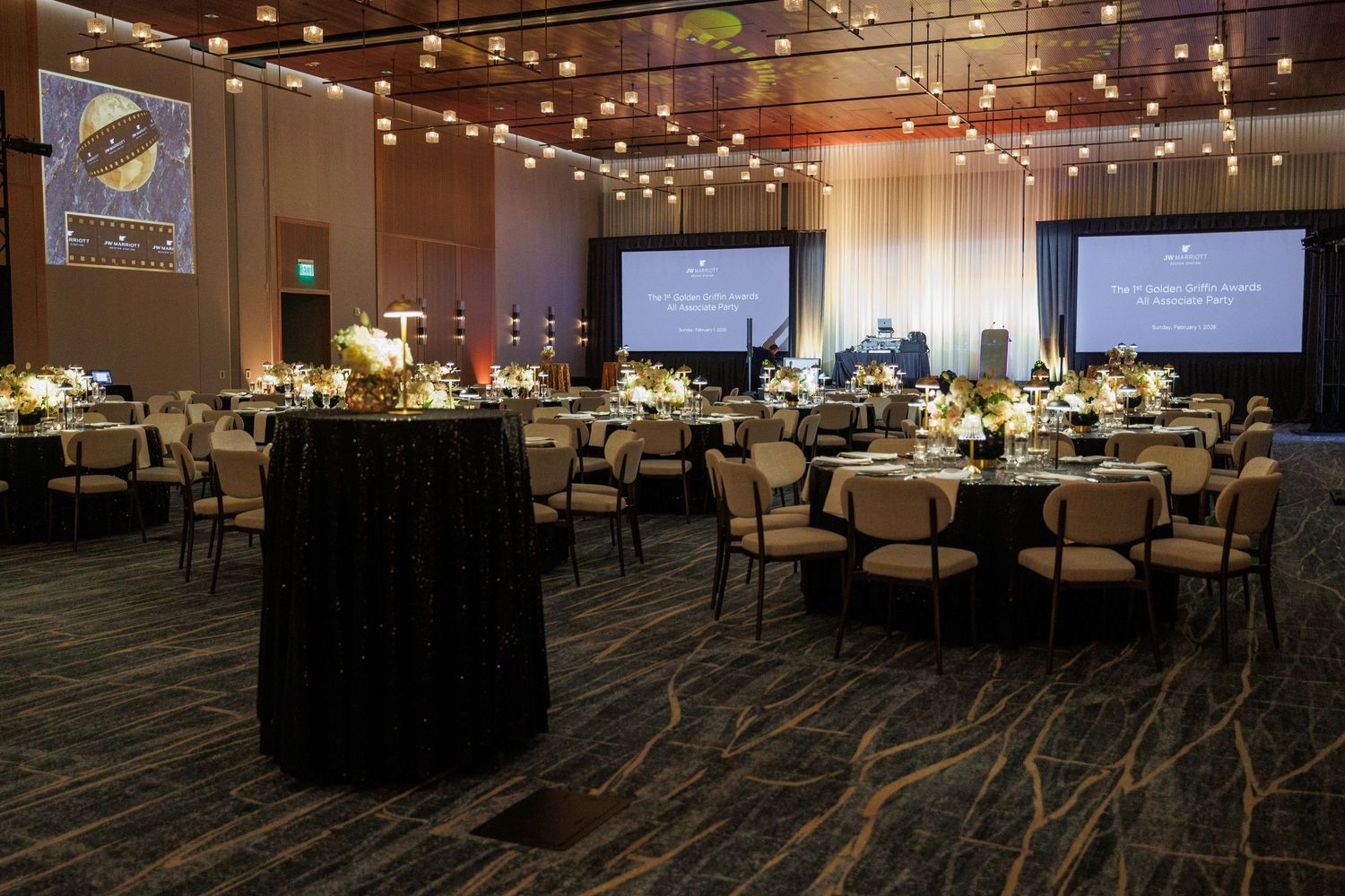 Elegant banquet hall with round tables, string lights, floral centerpieces, and dual projection screens for a formal event.