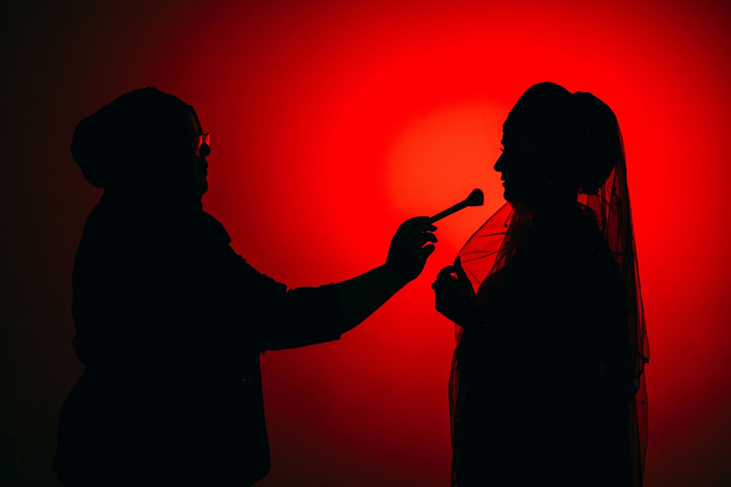 Silhouettes of two people in profile against a dramatic red background lighting up cigarettes.