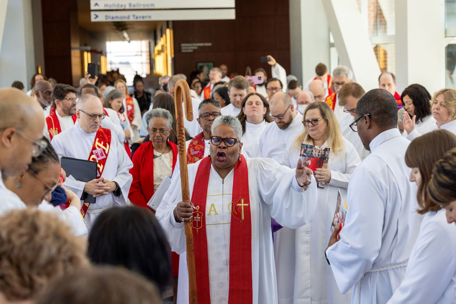 A group of clergy members in white robes and red stoles gather together during a religious ceremony.