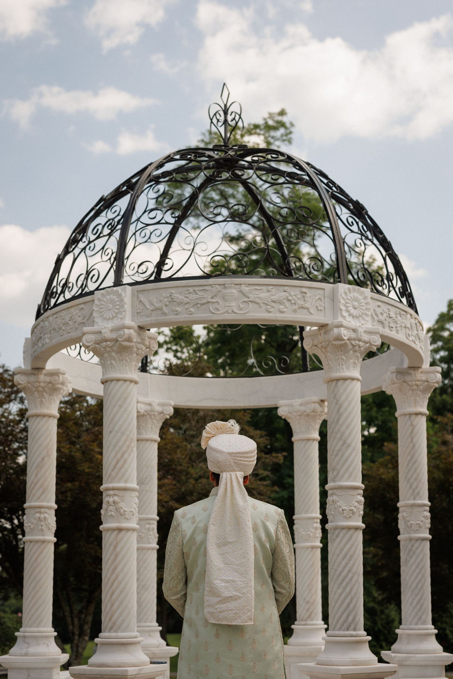A series of elegant white marble gazebos with ornate wrought iron domed tops set against a blue sky with clouds.