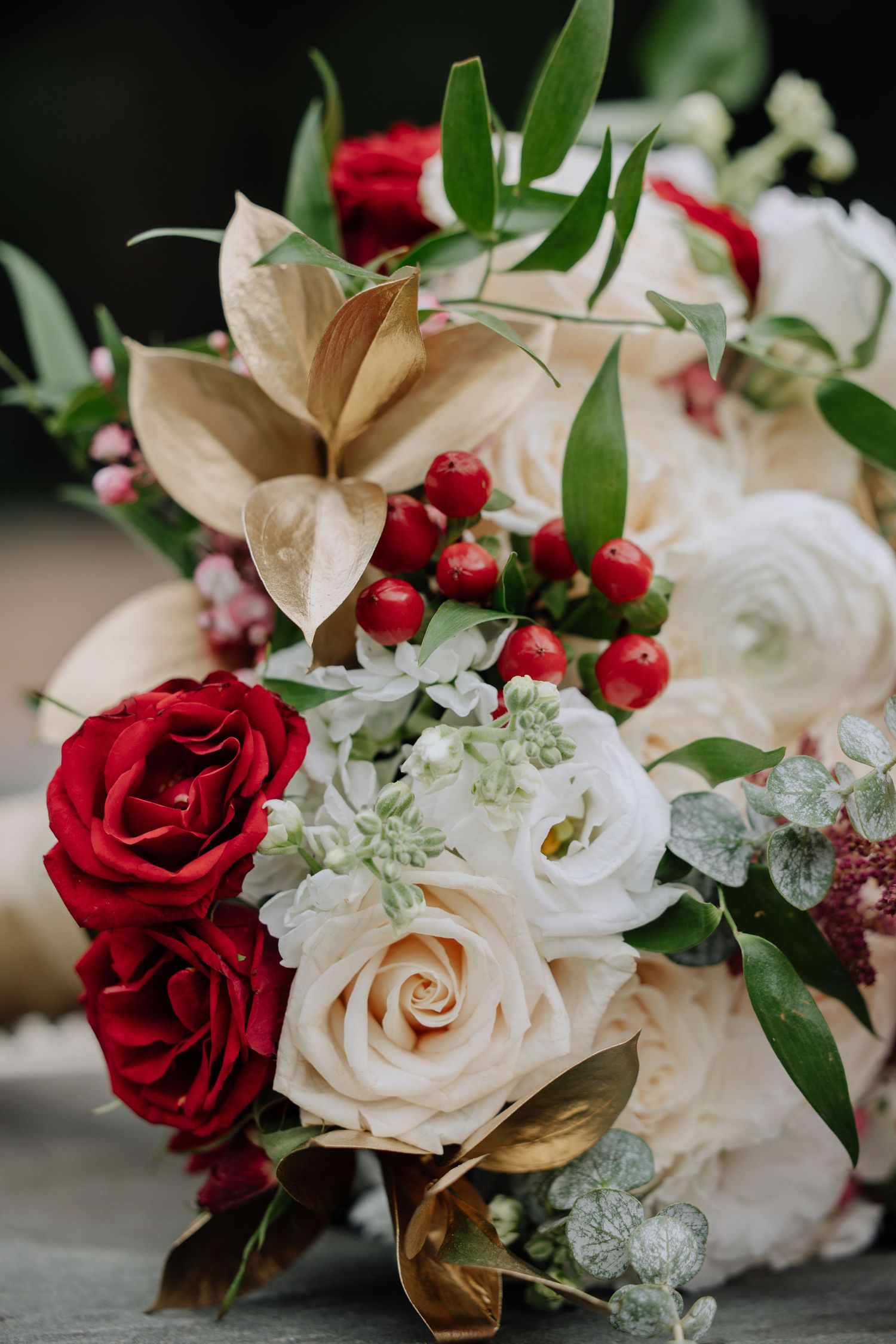 A romantic wedding bouquet featuring red and white roses with gold accents and delicate greenery arranged elegantly.