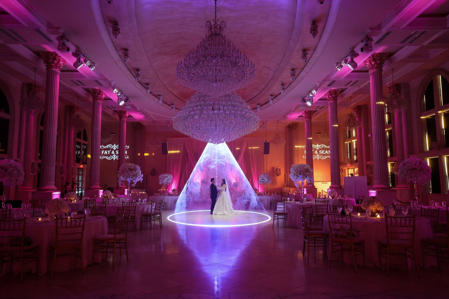 A grand ballroom illuminated in vibrant purple lighting with a glowing centerpiece creating an elegant atmosphere.