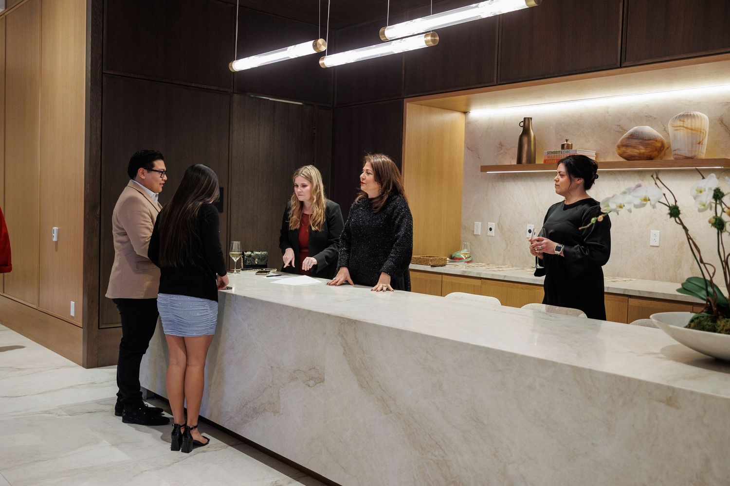 A group of people gathered around a modern white kitchen counter during a social gathering.