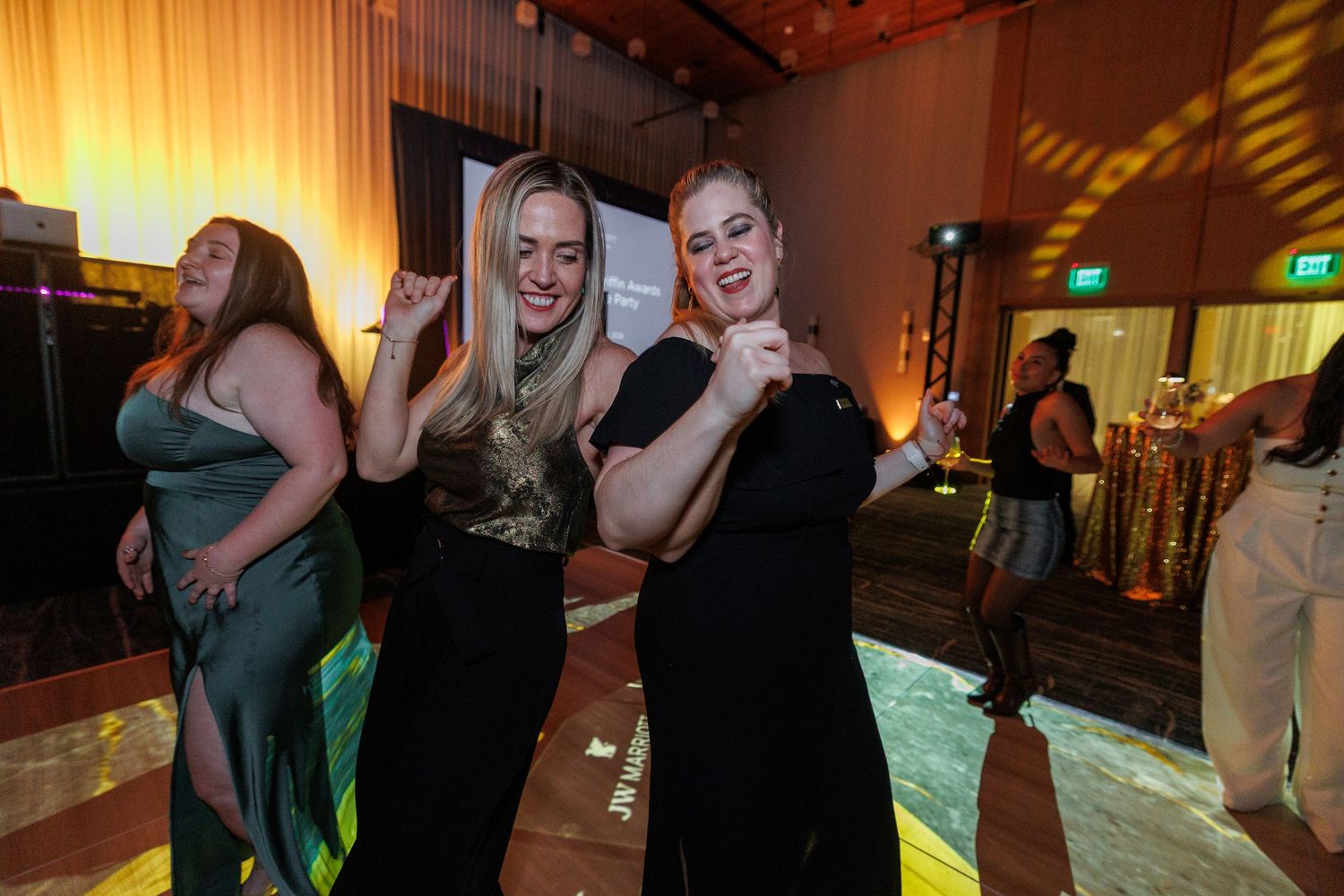 People dancing and having fun at a party with warm lighting and a dance floor.