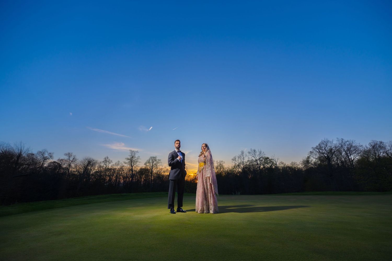 Couple standing on golf course at dusk with dramatic blue sky backdrop.