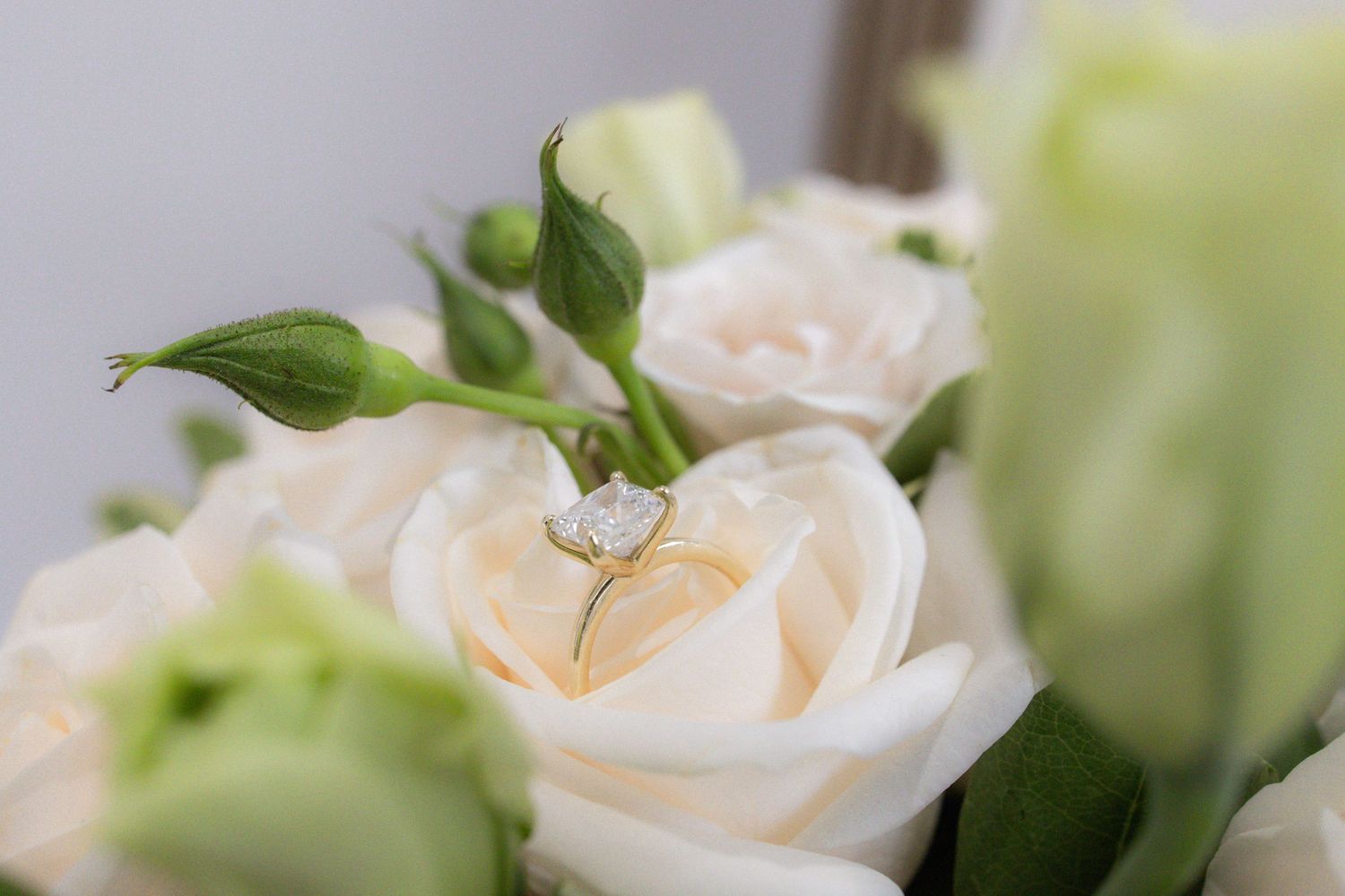 Diamond engagement ring nestled among white roses and green buds in a bridal bouquet.