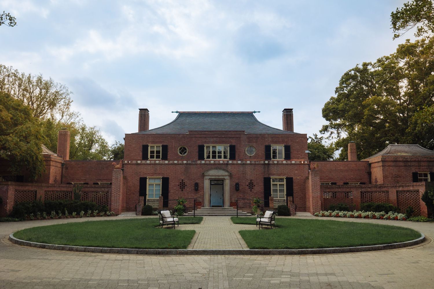 Panoramic view of a red brick university building complex with white columns and landscaped grounds on a cloudy day.