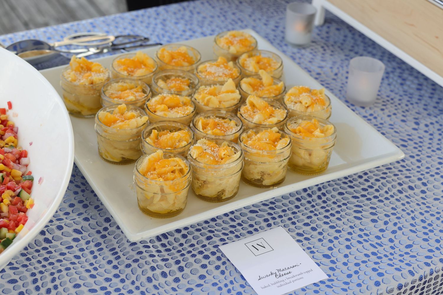 Elegant appetizer display featuring individual glass jars filled with creamy layered dip topped with shredded cheese on a white tray.