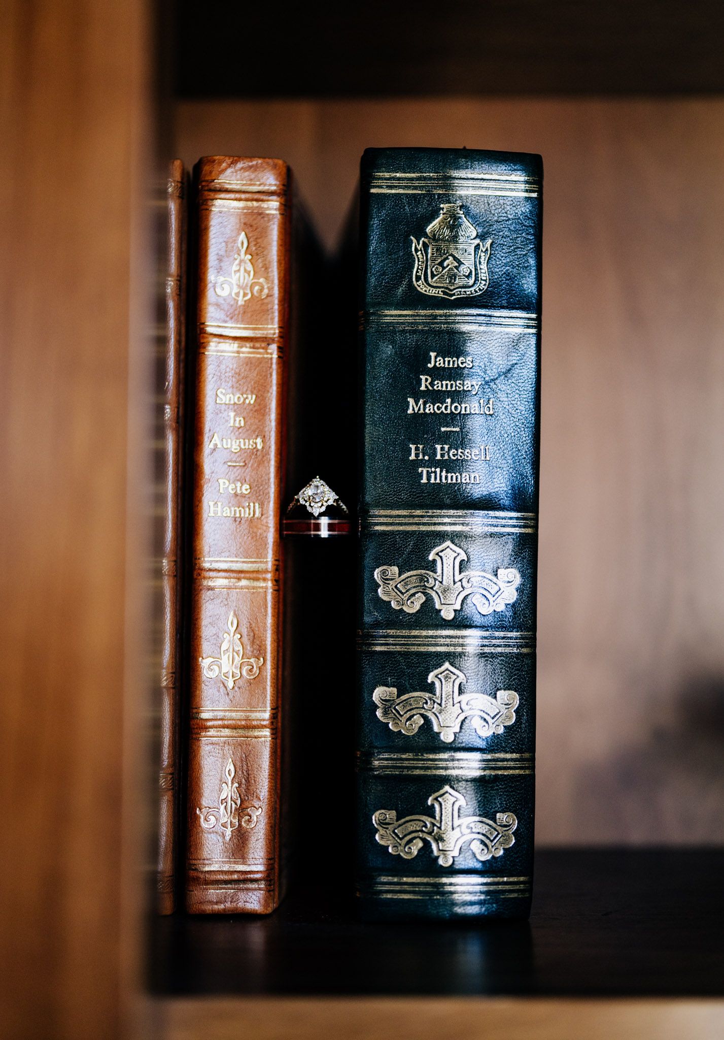 Vintage leather-bound books with ornate spines stand in a row on a wooden shelf with shallow depth of field.