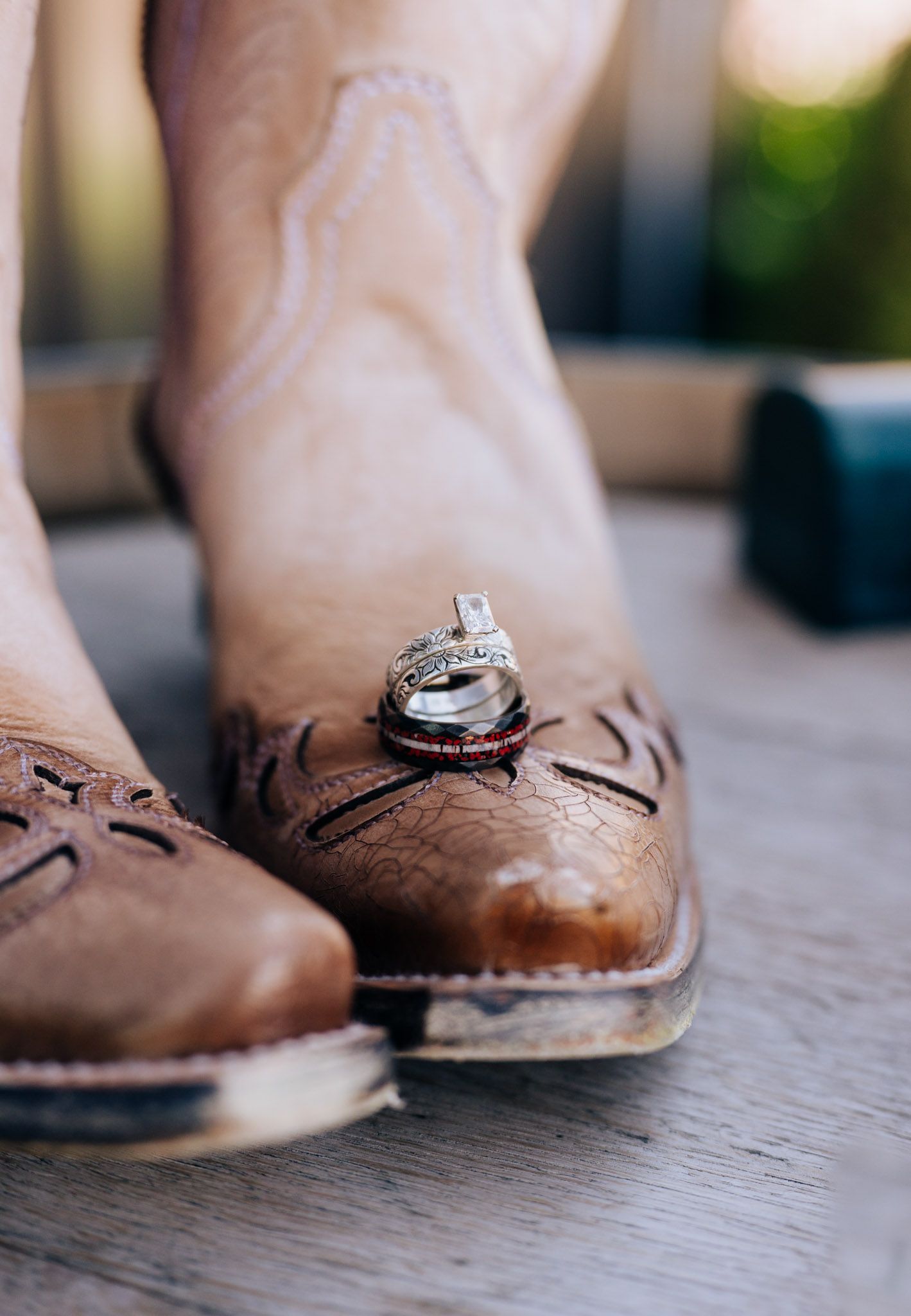 Wedding rings displayed on top of worn brown leather cowboy boots in a rustic country style setting.