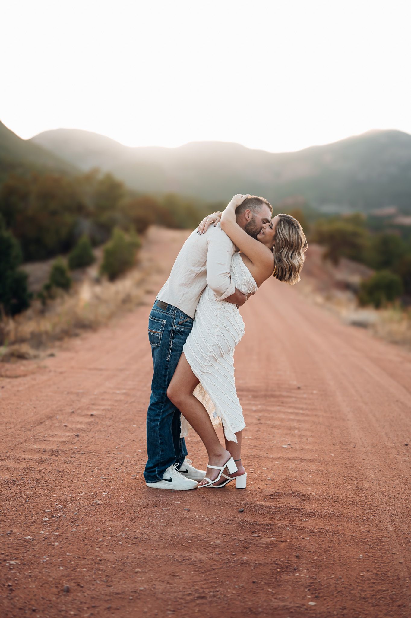 Romantic couple dances together on a dirt road in the desert mountains at sunset.