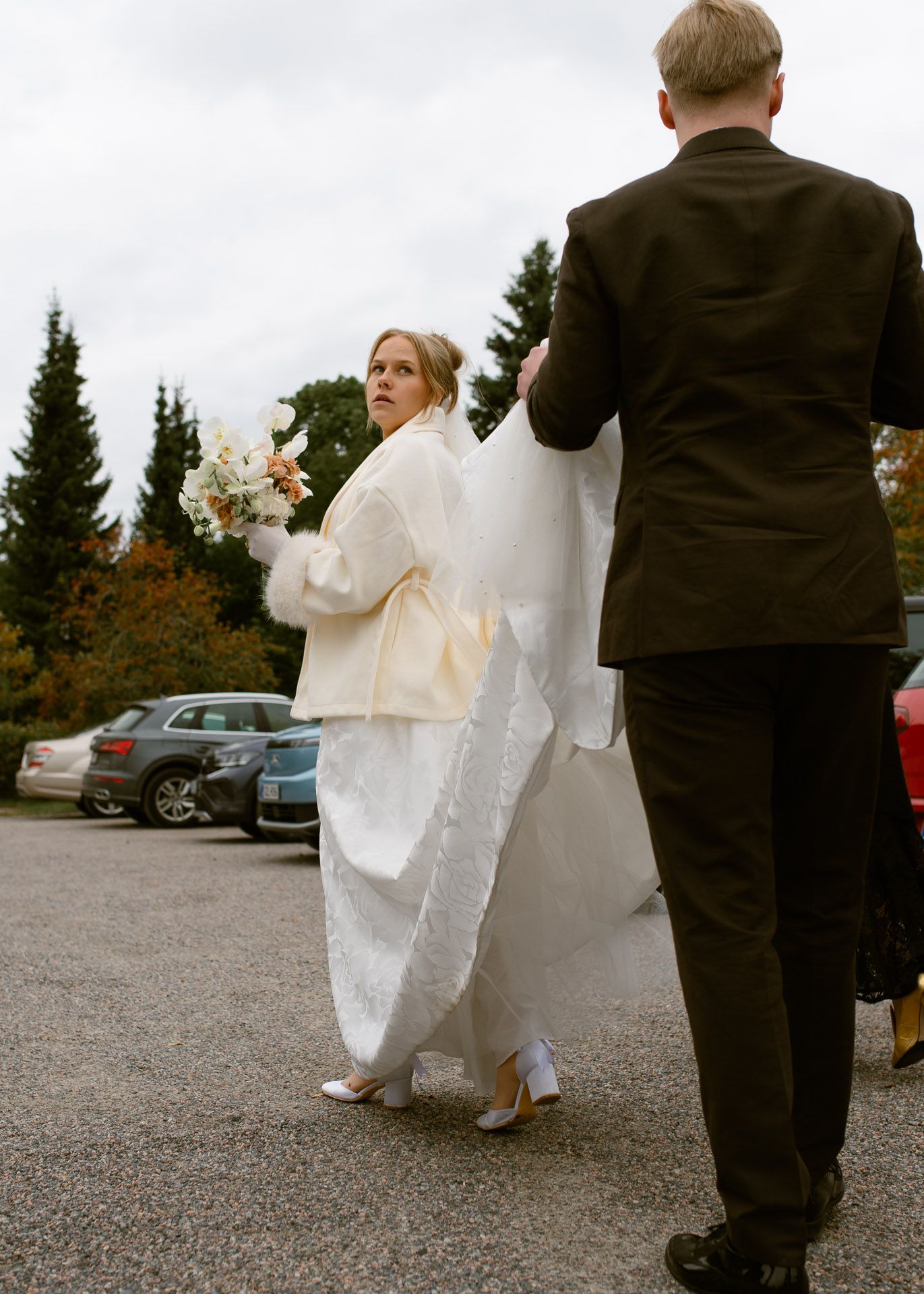 Sulhanen kannattelee morsiamen hääpuvun helmaa heidän kävellessään.