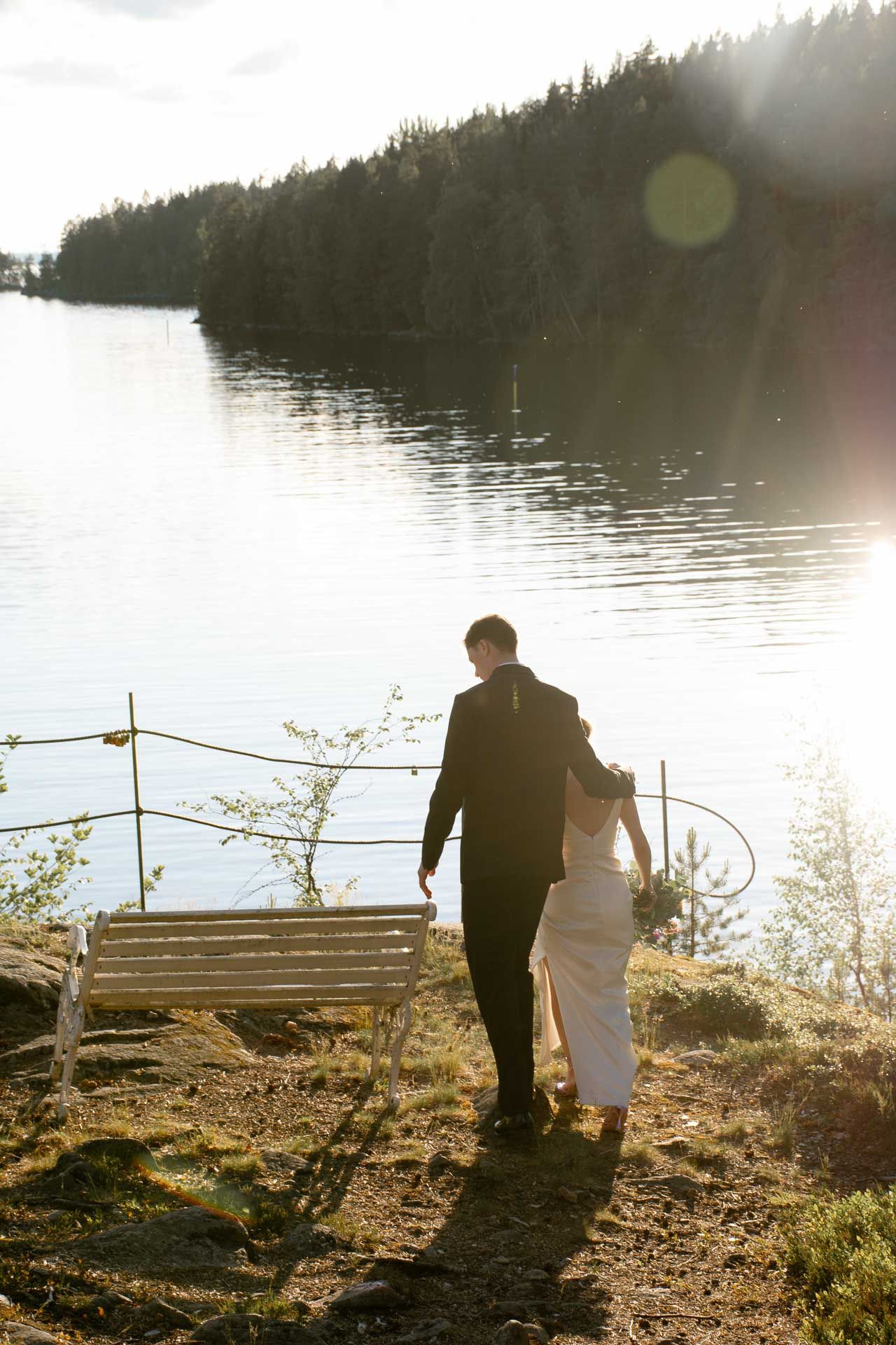 Hääpari menossa istumaan penkille järven rannalla.