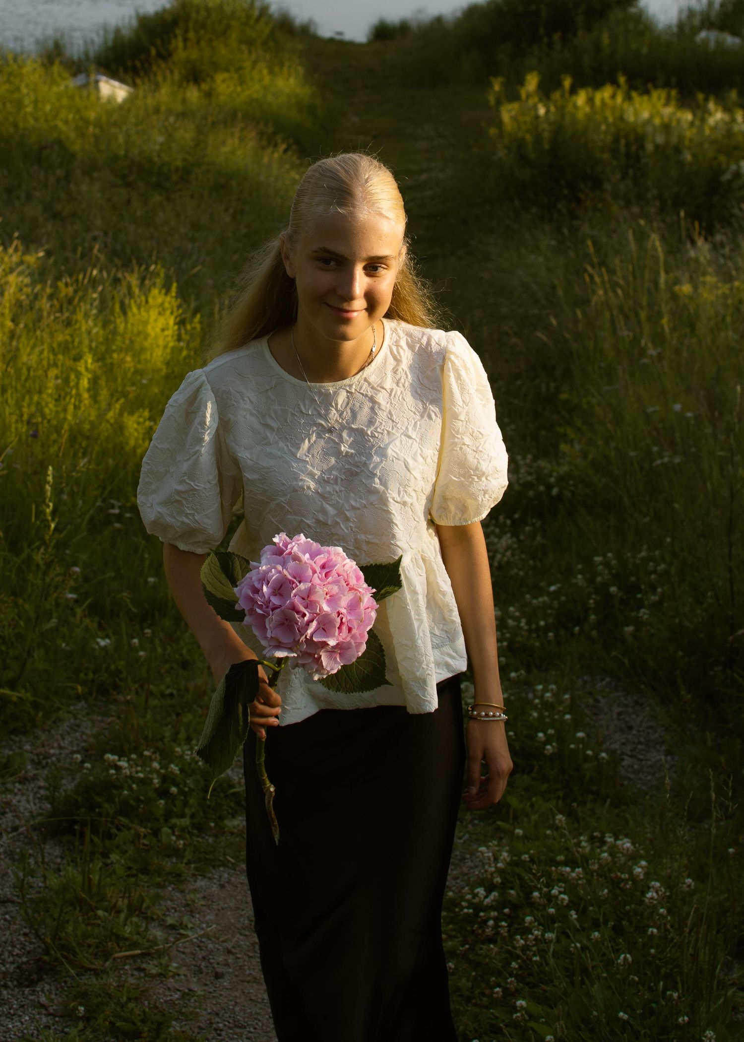 Konfirmoitu tyttö kukka kädessään elokuisessa illassa.