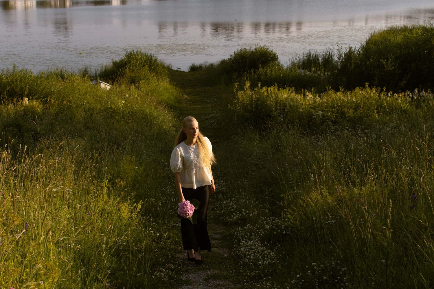 Konfirmoitu kävelee ilta-auringossa järven rannalla.