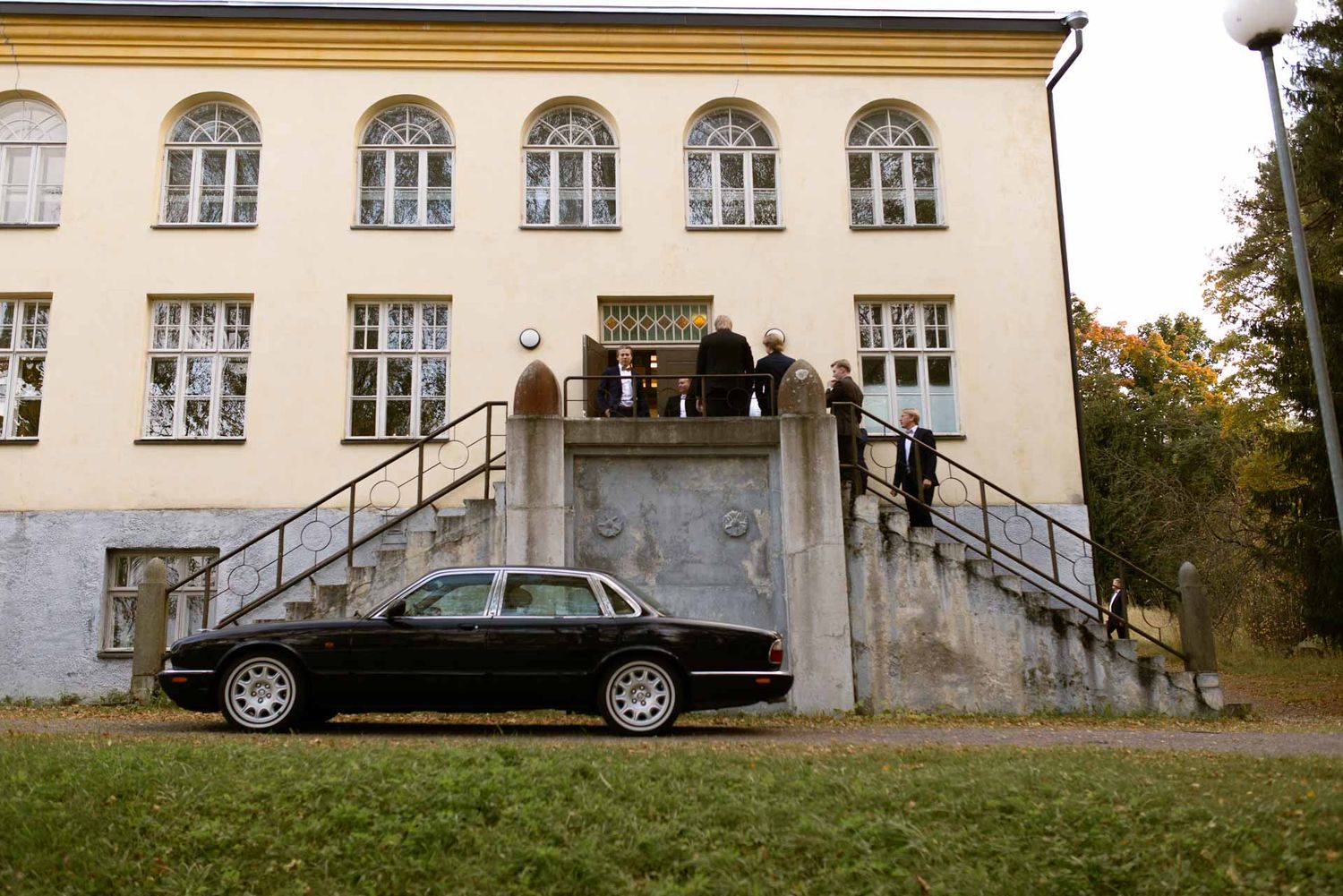 Hääauto ja vieraita juhlarakennuksen edustalla.