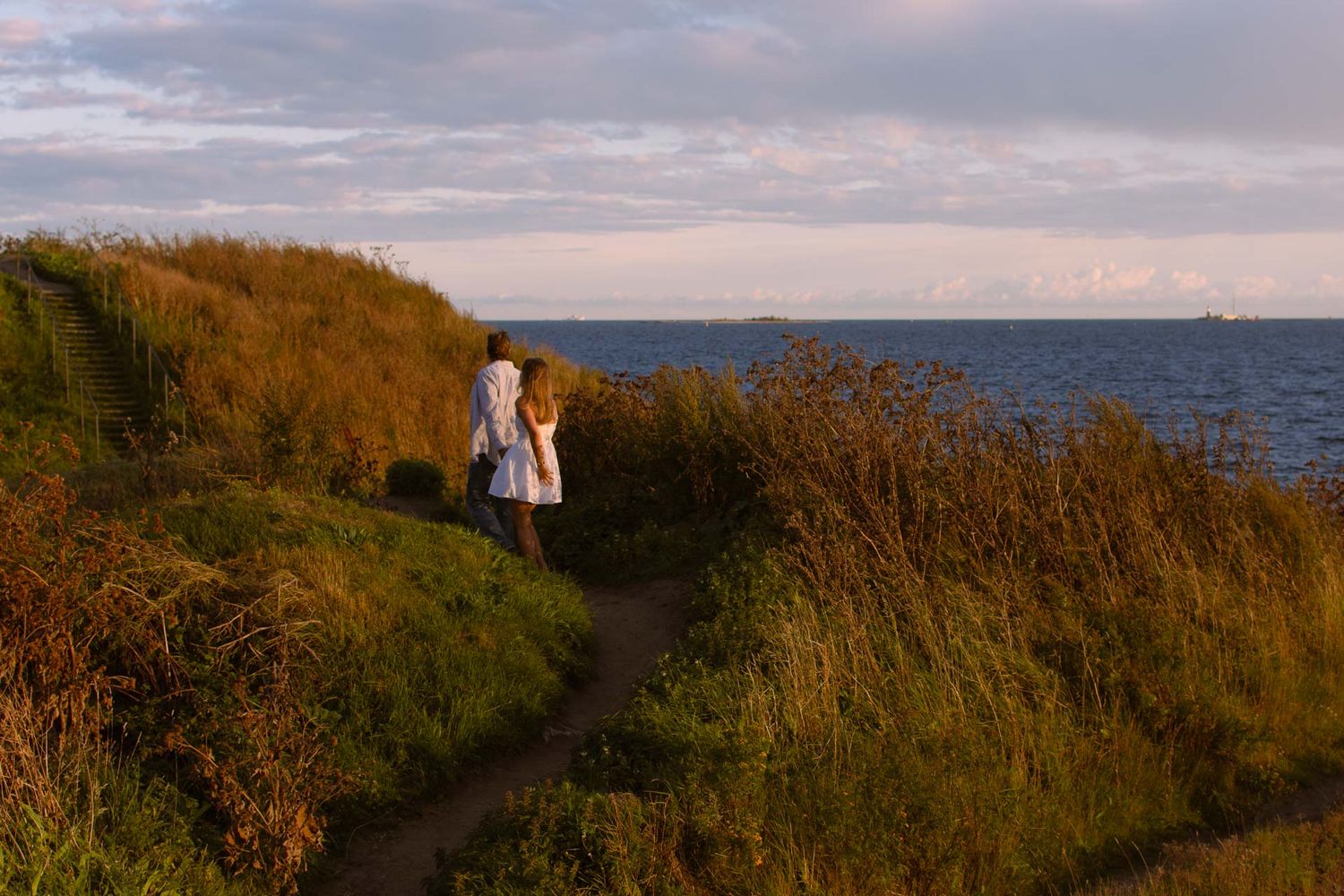 Pariskunta juoksee Suomenlinnan poluilla ilta-auringossa.