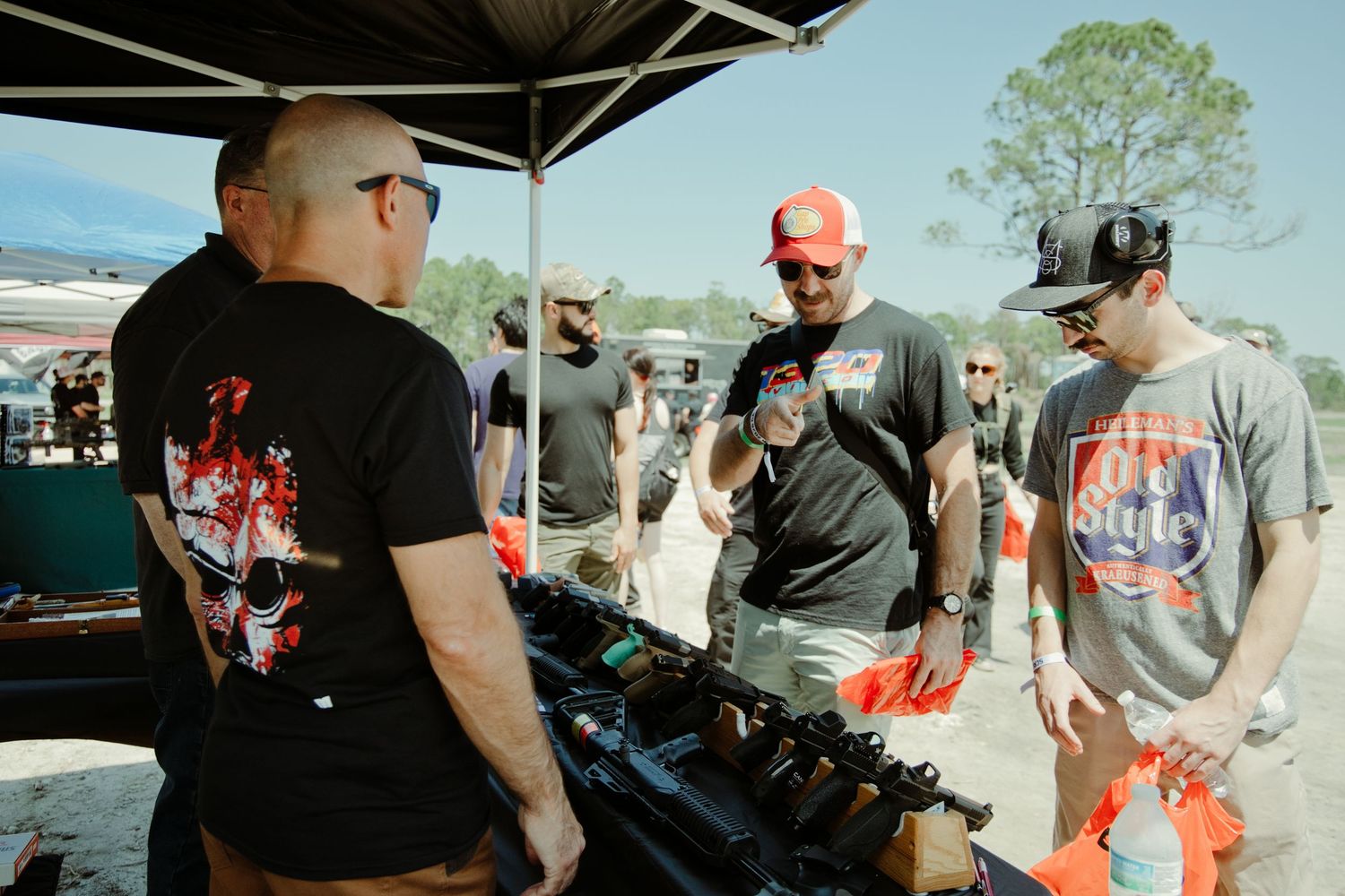 Gun enthusiasts examining firearms at an outdoor vendor booth during a range day event.