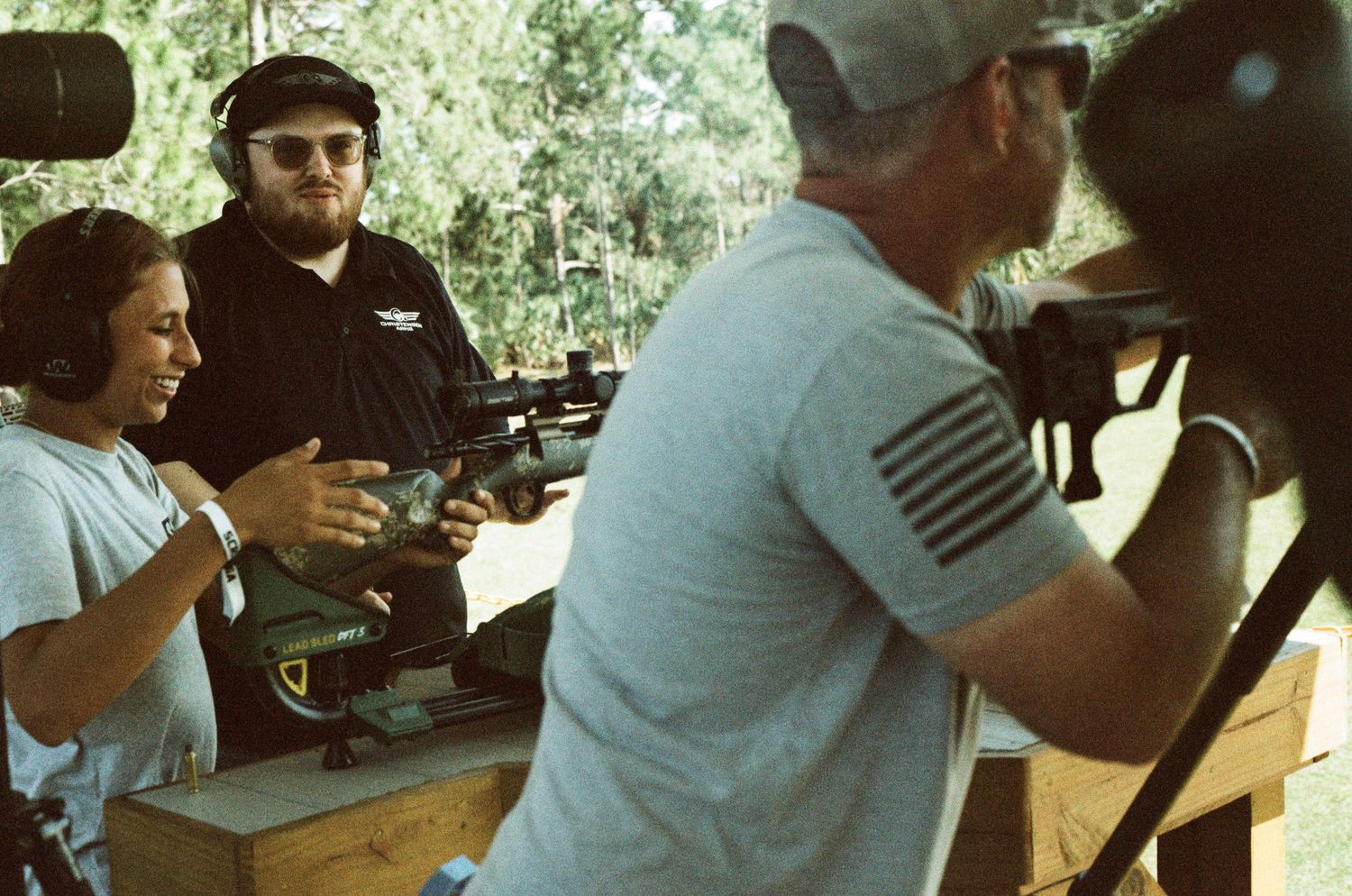 Instructor teaching a woman how to shoot an automatic rifle at an outdoor firearms training event.