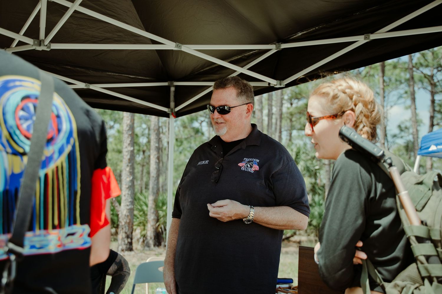 Event staff member in polo shirt conversing with attendees under a canopy at range day.