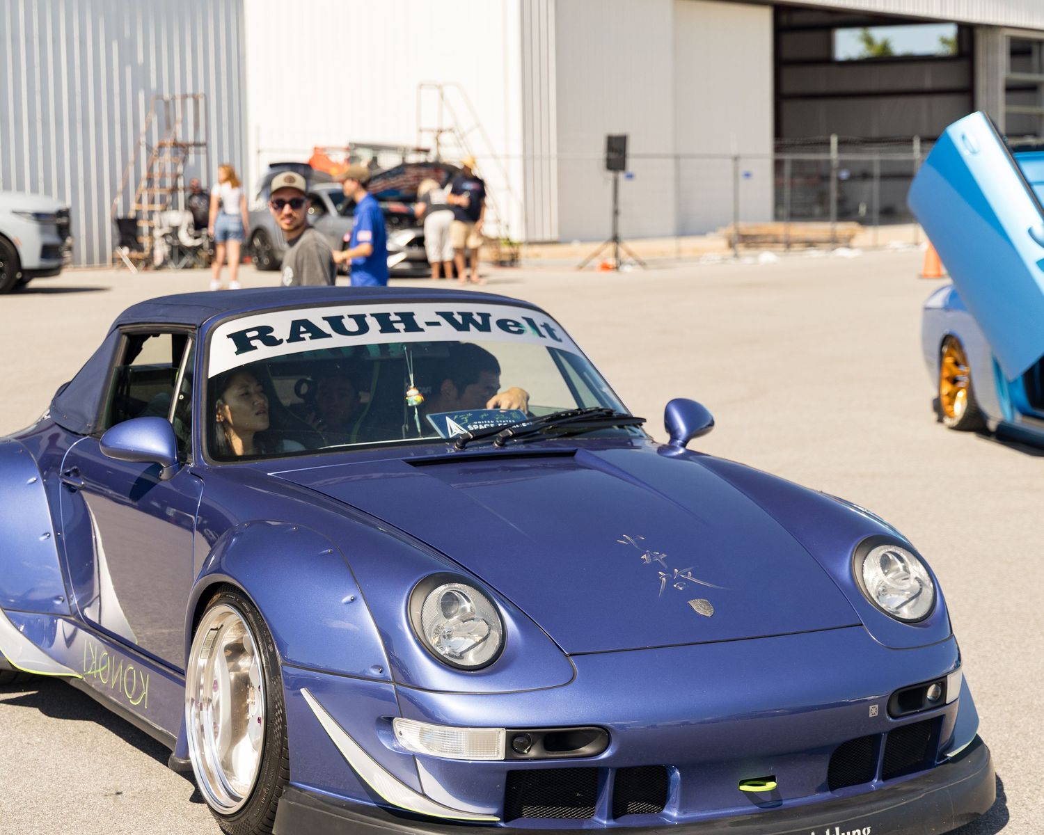 Modified blue Porsche 911 with Rauh-Welt Begriff bodykit parked at outdoor car meet.