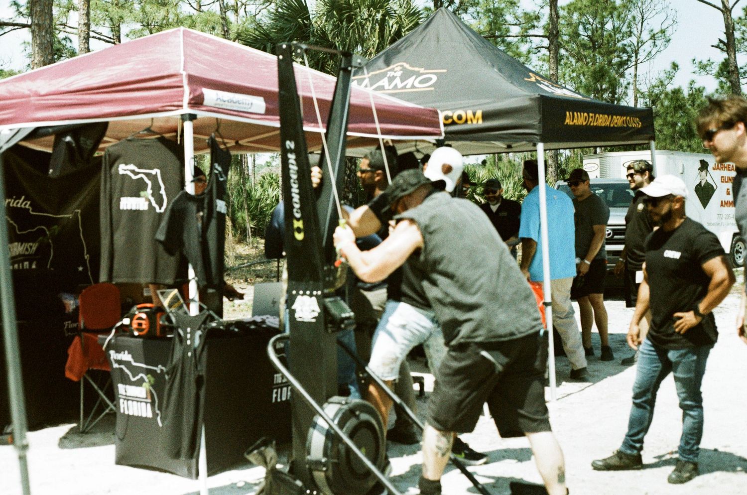 Vendors and attendees browse merchandise under dark red and gold canopy tents at an outdoor market event.