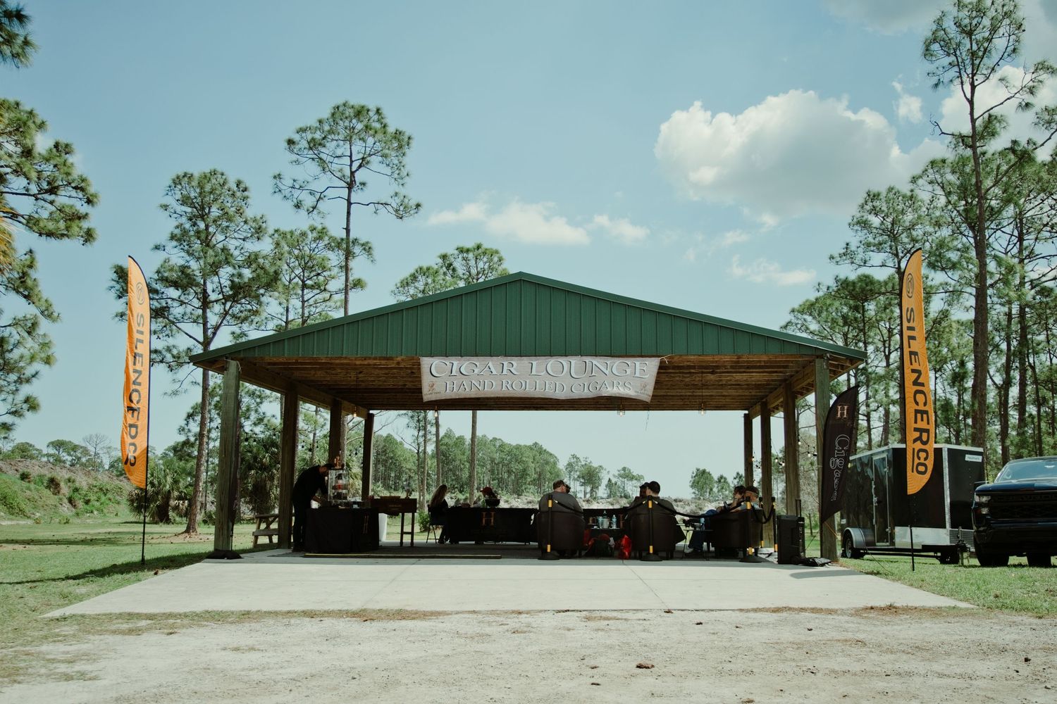 Outdoor covered pavilion stage setup surrounded by pine trees at a rural shooting event venue.