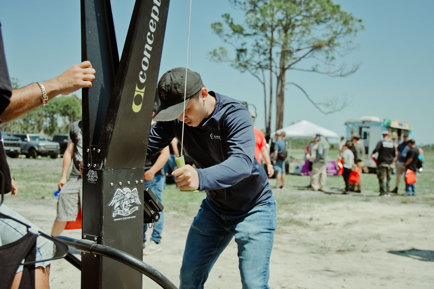Person leaning over a Concept2 rowing machine at an outdoor fitness event on a sunny day.