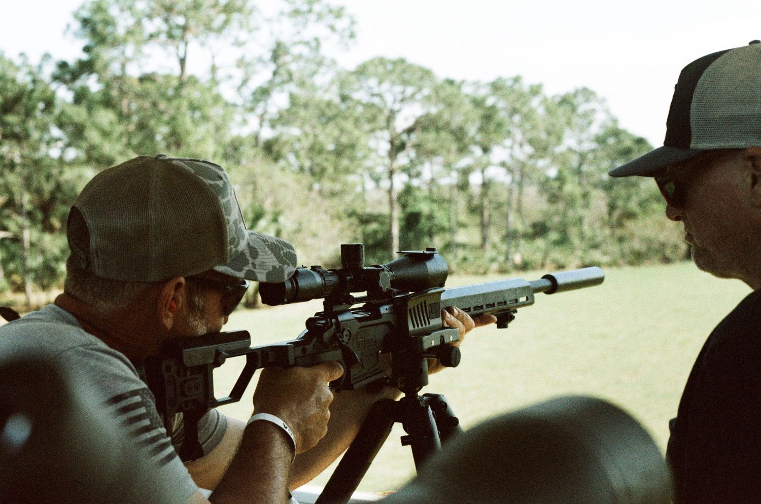 Person aiming a scoped AR-15 rifle at an outdoor shooting range.