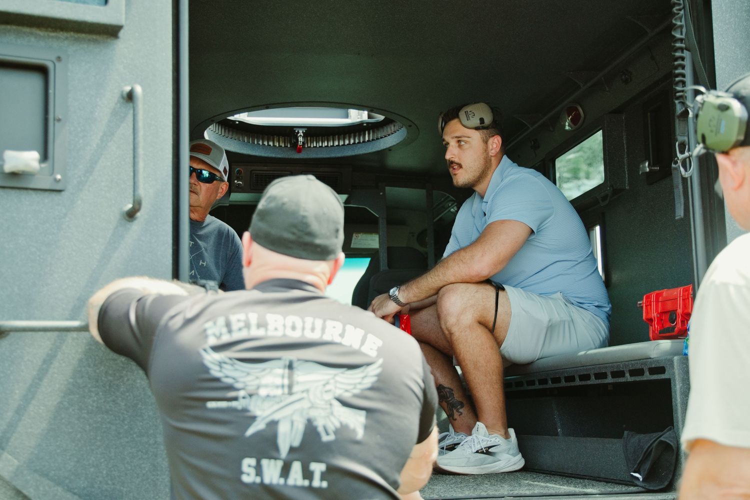 Men sitting inside a Melbourne SWAT tactical vehicle during an outdoor event.