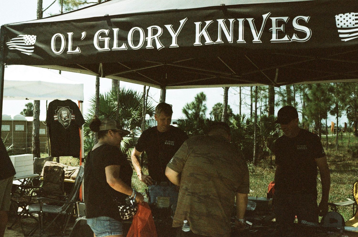 Ol Glory Knives vendor booth with customers browsing knives under a canopy at outdoor expo.