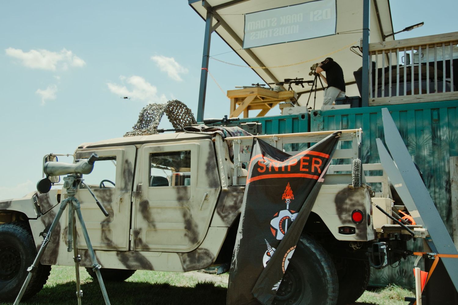 Military Humvee with camouflage and sniper rifle on display at an outdoor event.