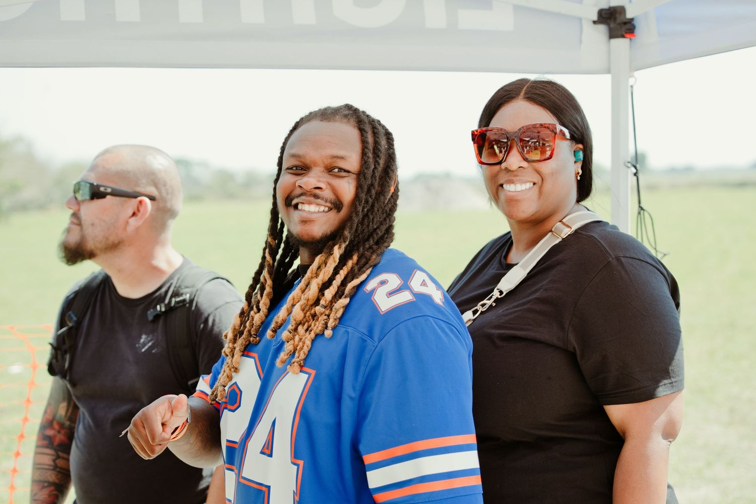 Two smiling people pose under a tent at an outdoor event, one wearing a blue jersey number 24.