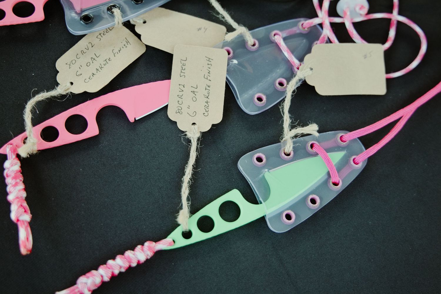 Colorful handmade knife sheaths with price tags displayed on a table at an outdoor market or gun show.