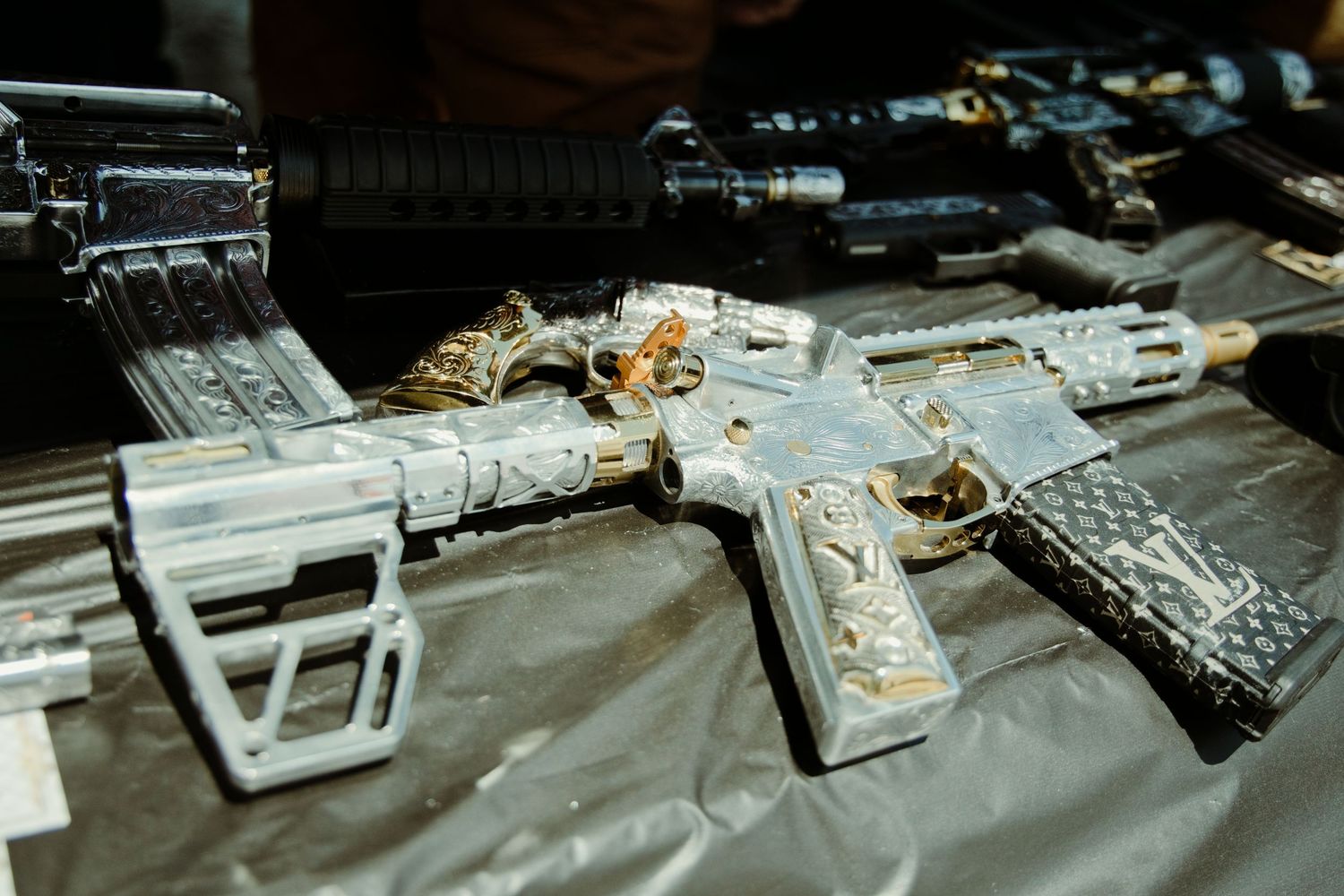 Decorative custom AR-15 rifle with gold and silver engraving displayed at an outdoor gun expo.