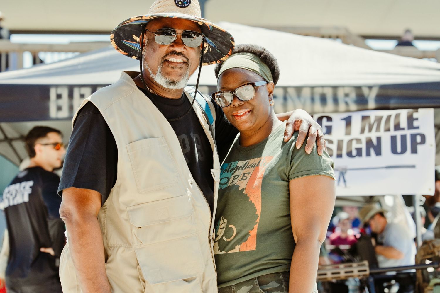 Two people smiling together under a tent at an outdoor firearms and shooting sports event.