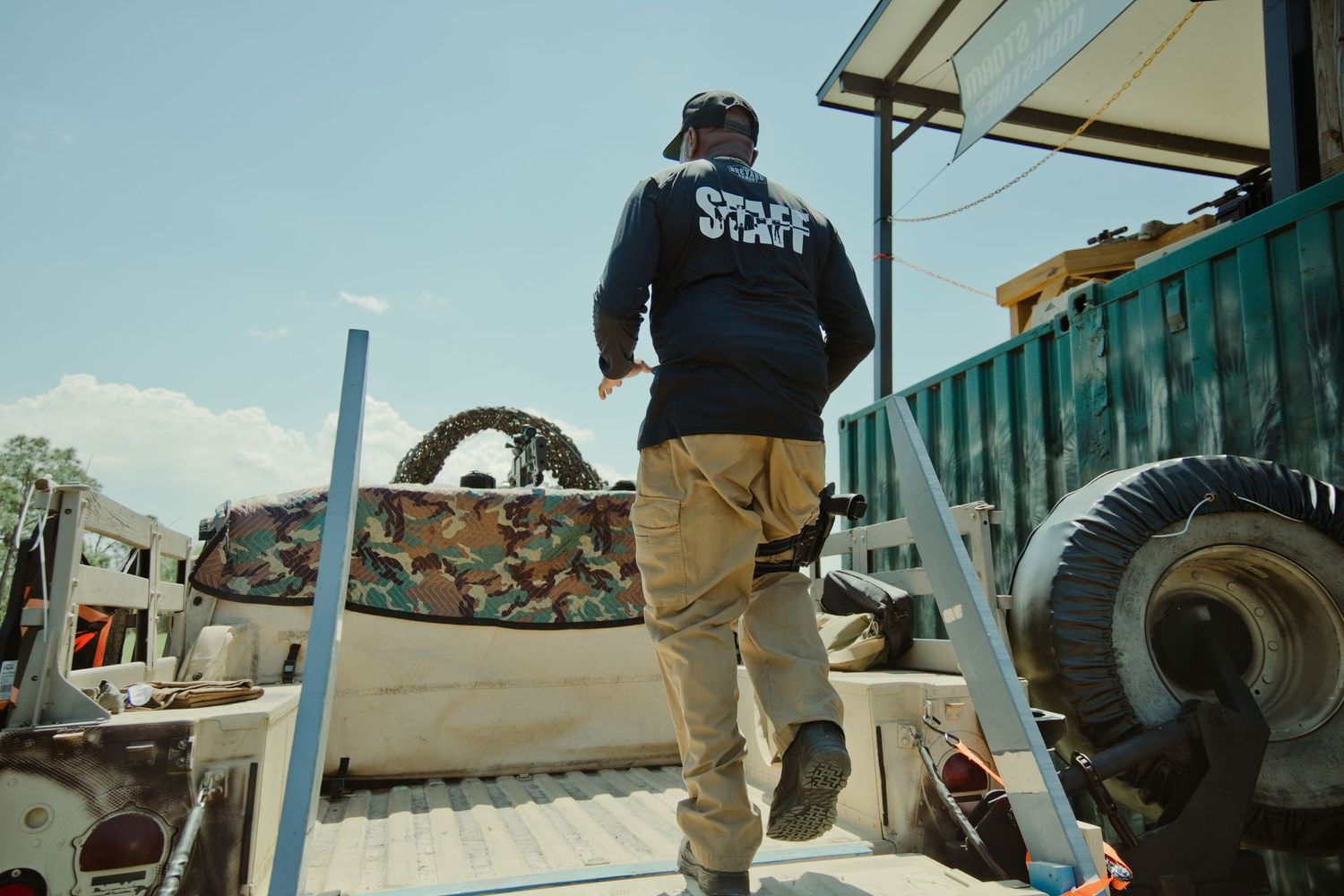 A worker in a blue jacket climbs a ladder onto a truck bed filled with industrial equipment outdoors.