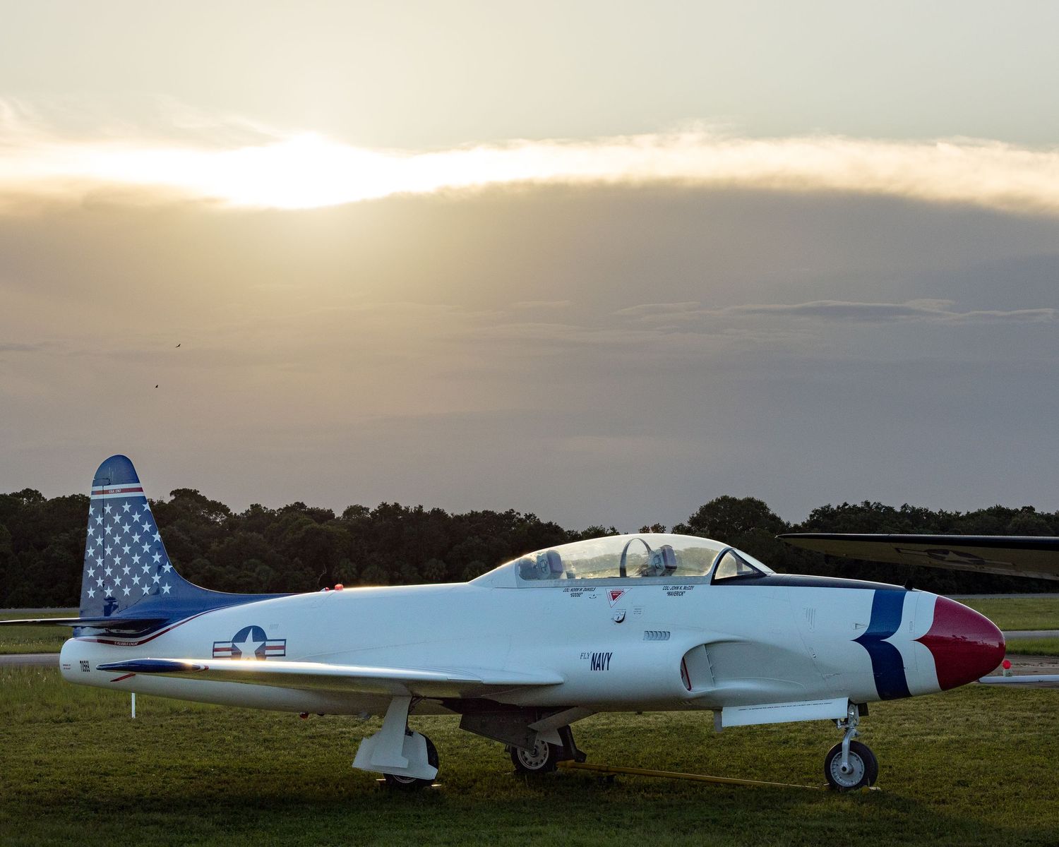 Vintage military aircraft parked on airfield tarmac during sunset.