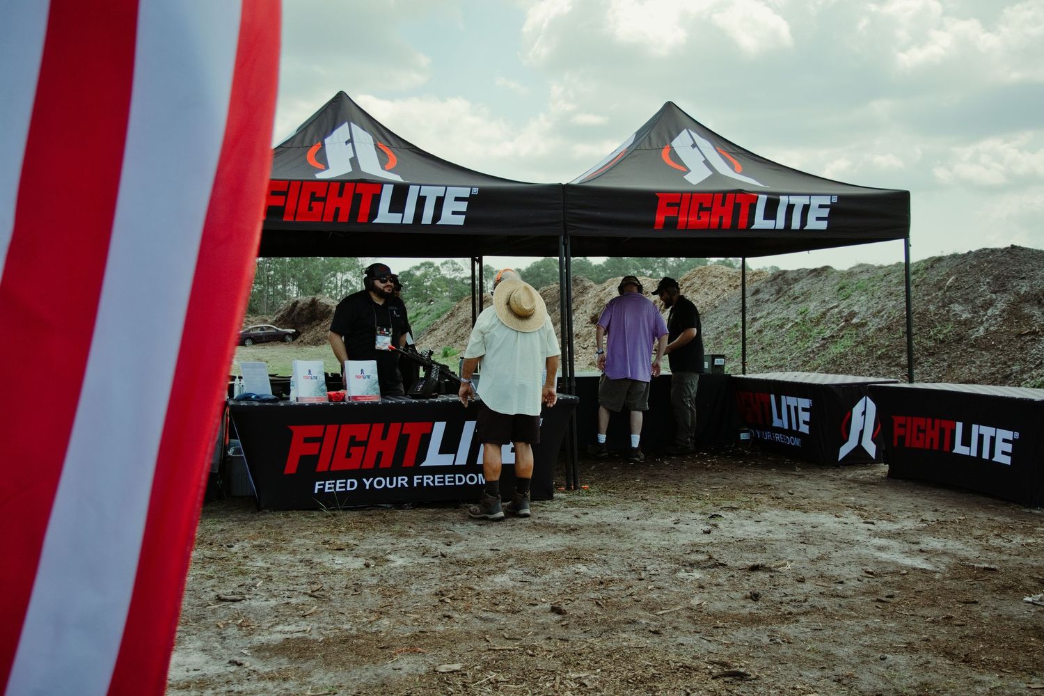 FightLite branded canopy tents set up at an outdoor shooting range event with vendors and attendees.