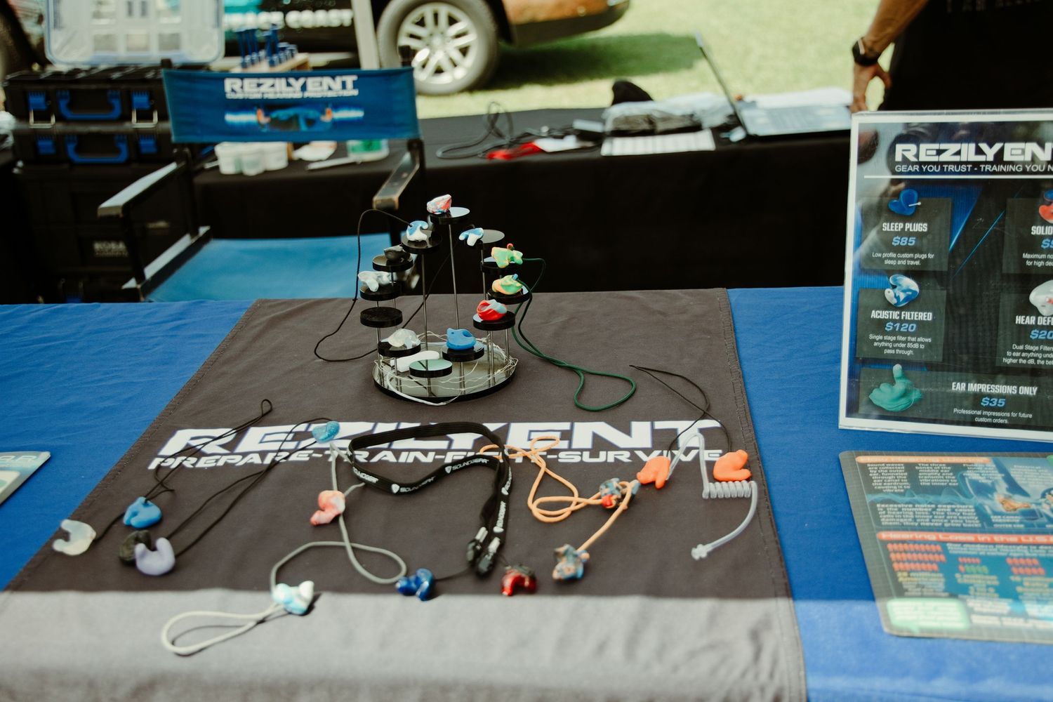 Rezlyent survival gear display table with paracord bracelets and accessories at an outdoor expo event.
