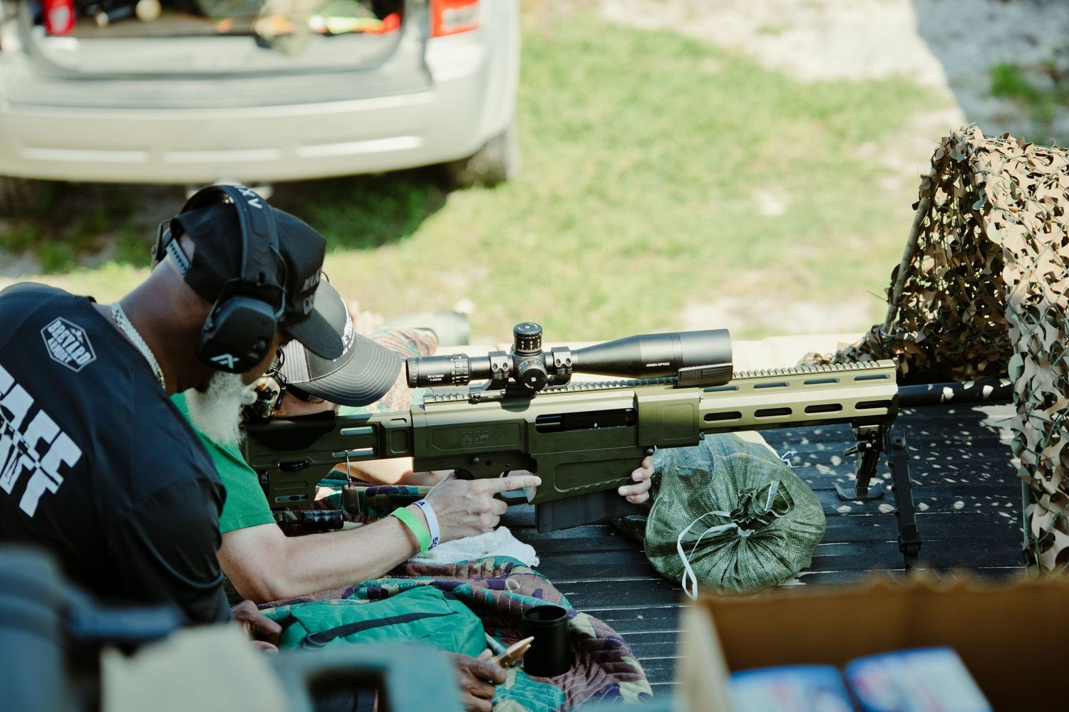 Shooter in prone position aiming a scoped precision rifle at an outdoor long-range shooting event.