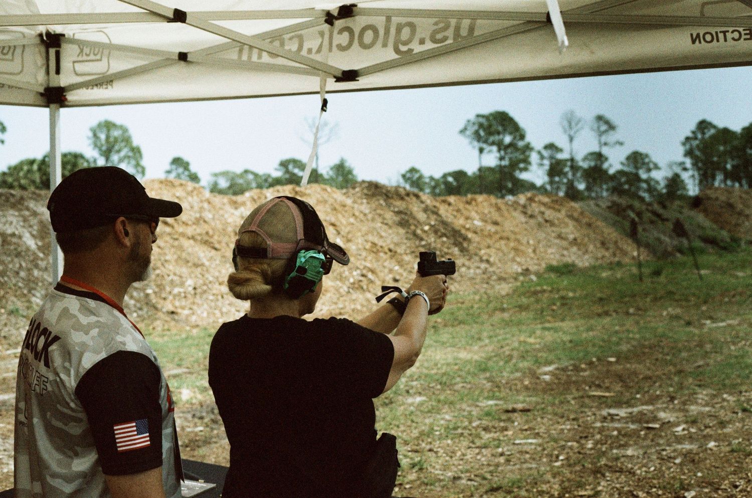 Two people practicing pistol shooting at an outdoor gun range under a Glock tent.