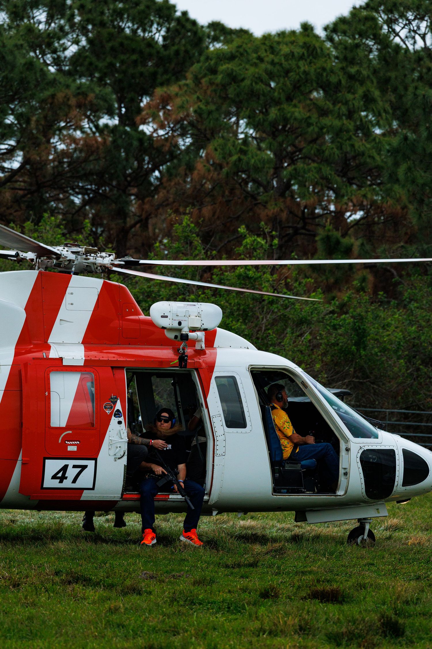 Red and white helicopters parked on grassy field with crew members nearby.